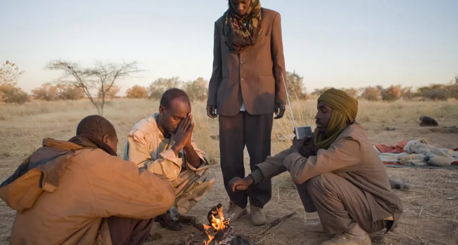 Men sit by fire and communicate through radio