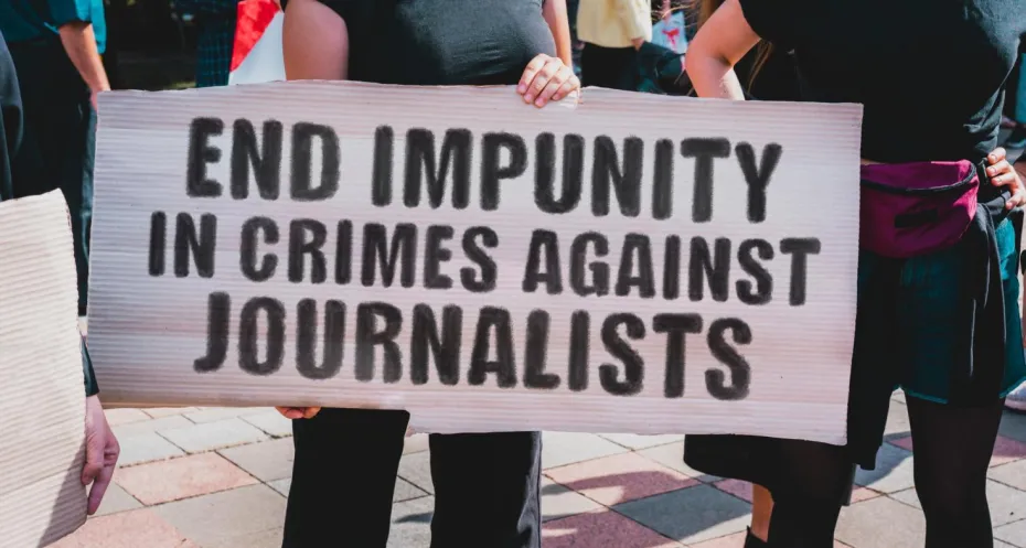 woman holds plate with protest against impunity for crimes against journalists.