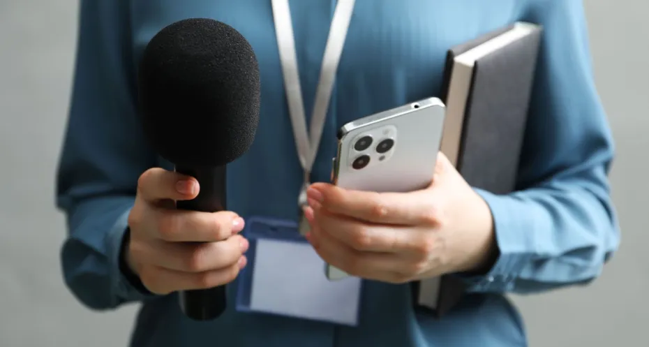 Journalist met een microfoon, notitieboek en telefoon.